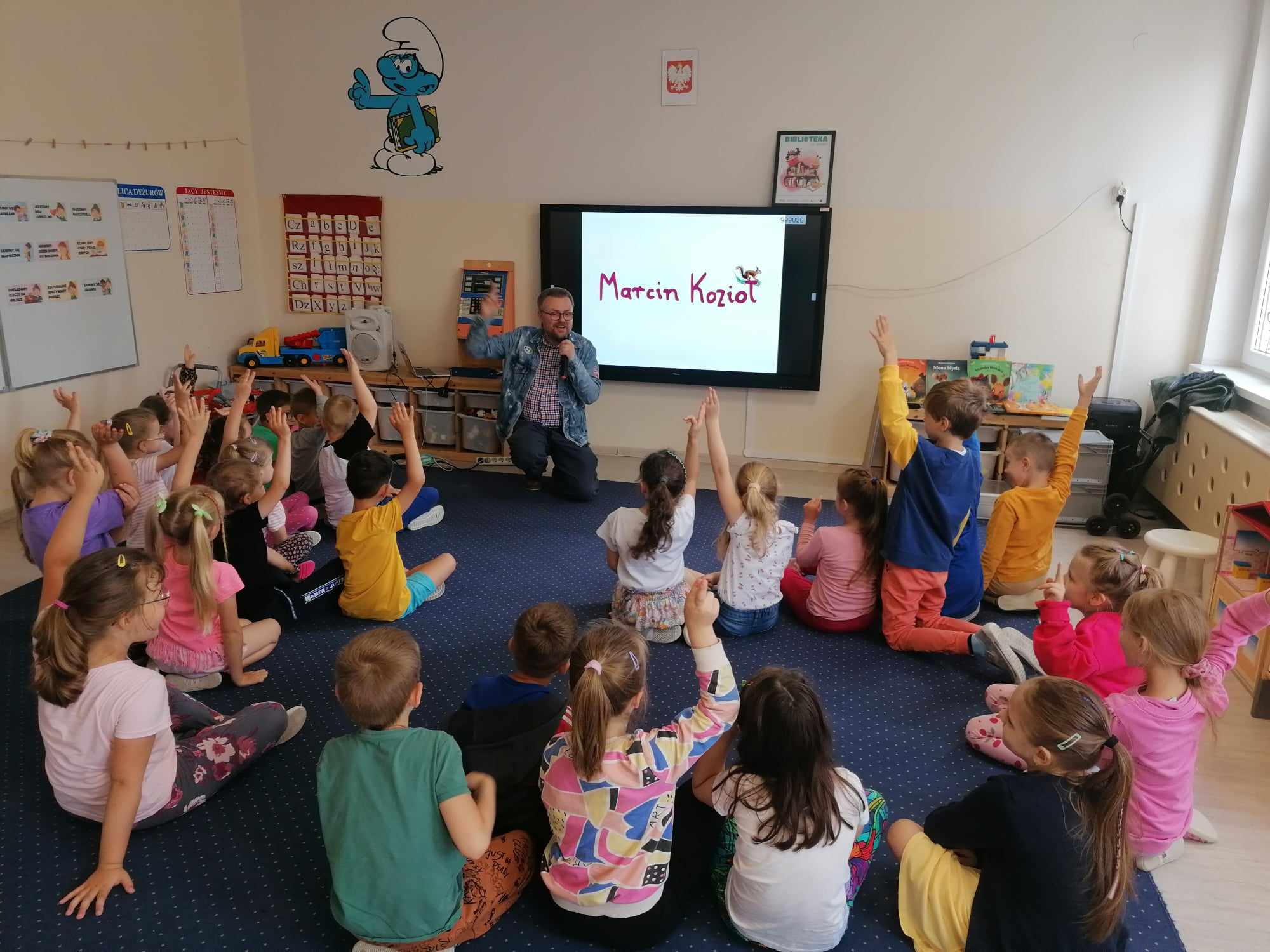 Autor książek z grupą dzieci przed tablicą multimedialną.