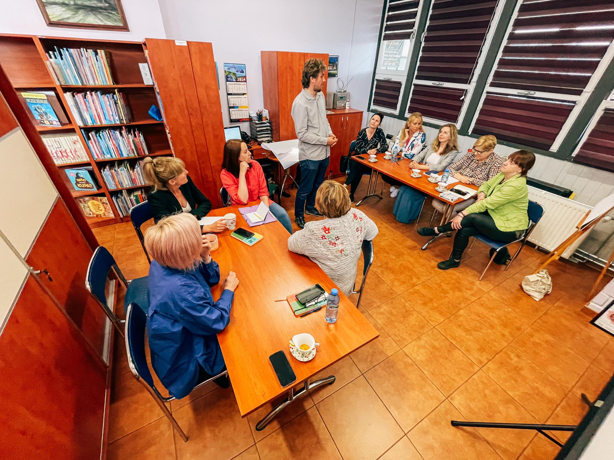 Grupa osób siedzących przy stole i słuchających wykładowcy.